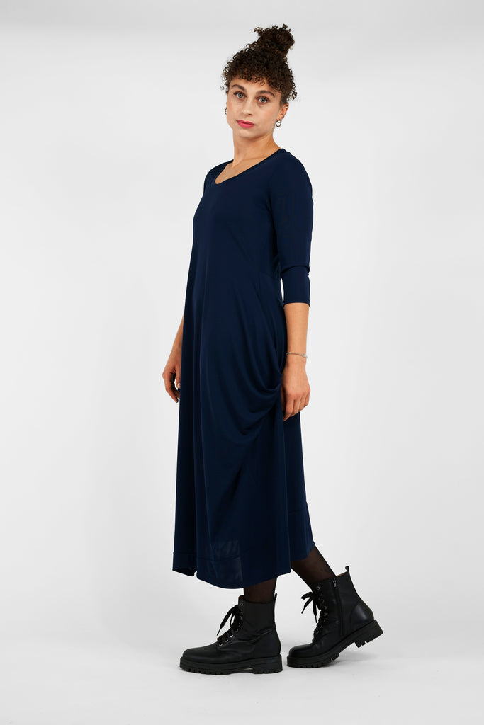 Feminin, schick, elegant aber zugleich lässig-casual.   Das Midi-Kleid aus fließendem, bi-elastischem Stoff sorgt für eine feminine Silhouette, hat aber zugleich lässige Eigenschaften: mit modisch gerafften Details unterhalb der Seitennahttaschen, weitem Rundhalsausschnitt und 3/4 Ärmeln. Hinten befindet sich eine mittige Naht, die Saumlinie vorne ist leicht abgerundet und verlängert. 